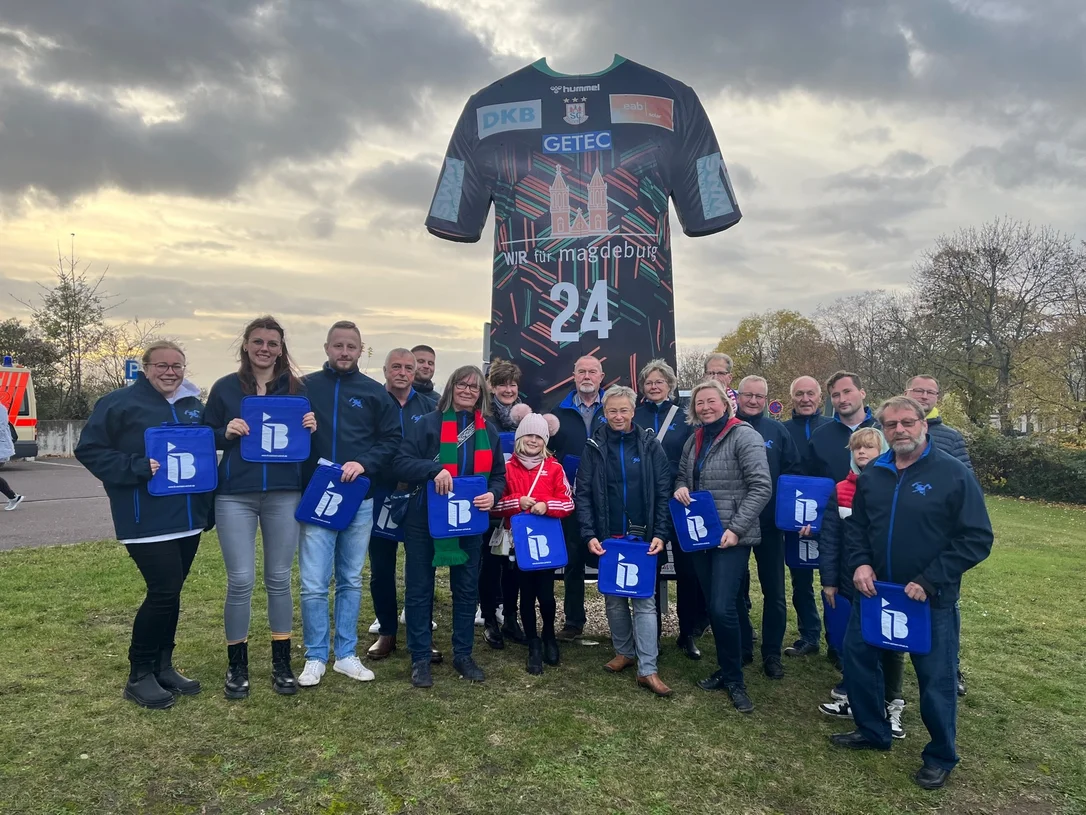 Mitglieder des Förderverein Schernickau mit IB-Logos in der Hand vor einer Arena in Magdeburg