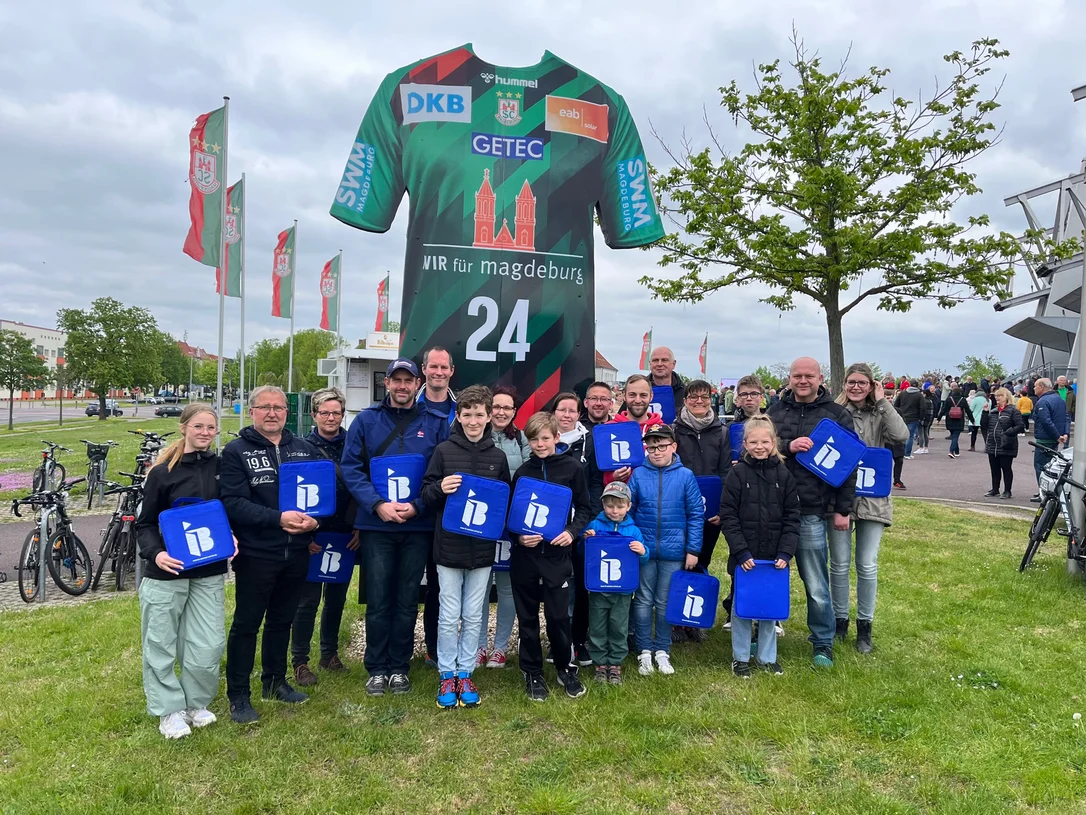 Mitglieder des Förderverein der Ortsfeuerwehr Biere mit IB-Logos in der Hand vor einer Arena in Magdeburg